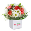This striking bouquet, styled with a blend of artistry and neighbourly warmth, sits proudly in a pristine white gift bag-evoking the welcoming spirit of Harold Wood. Ruffled carnations in coral, peach, and lively red provide a lush, textured heart, conjuring echoes of Harold Wood's community gardens and springtime hedgerows. Dotting the bouquet, crisp white daisies with radiant yellow-green centers impart an uplifting, sunlit cheer, while delicate sprigs of baby's breath weave through like sparkling morning dew. Subtly entwined, hints of unopened purple buds add depth and a quiet sense of anticipation, suggesting the beauty of blooms yet to come. All are encircled by deep, glossy green foliage-broad and arching leaves whose sheen and richness mirror the verdant landscape that defines the local area. The arrangement is shaped to a perfect, rounded fullness, promising both abundance and care. Sturdy white ribbon handles on the modern gift bag make for easy carrying, ideal for a birthday surprise or a congratulatory delivery along Gubbins Lane. Captured in the clarity of a pure white setting, every shade and texture stands out, highlighting the freshness and vibrant life of the flowers. This bouquet reflects the artistry and hospitality of a dedicated Harold Wood florist-a gift designed to brighten moments and bring heartfelt cheer to loved ones across the neighbourhood.
